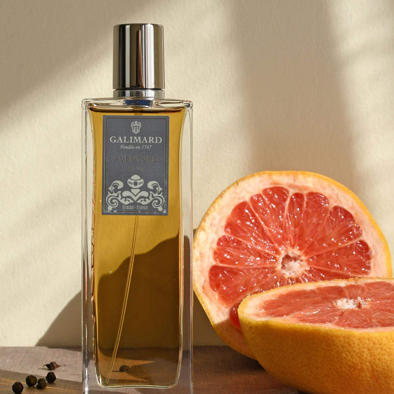 Perfume Aventure de Galimard junto a un pomelo partido en 2 y pimienta