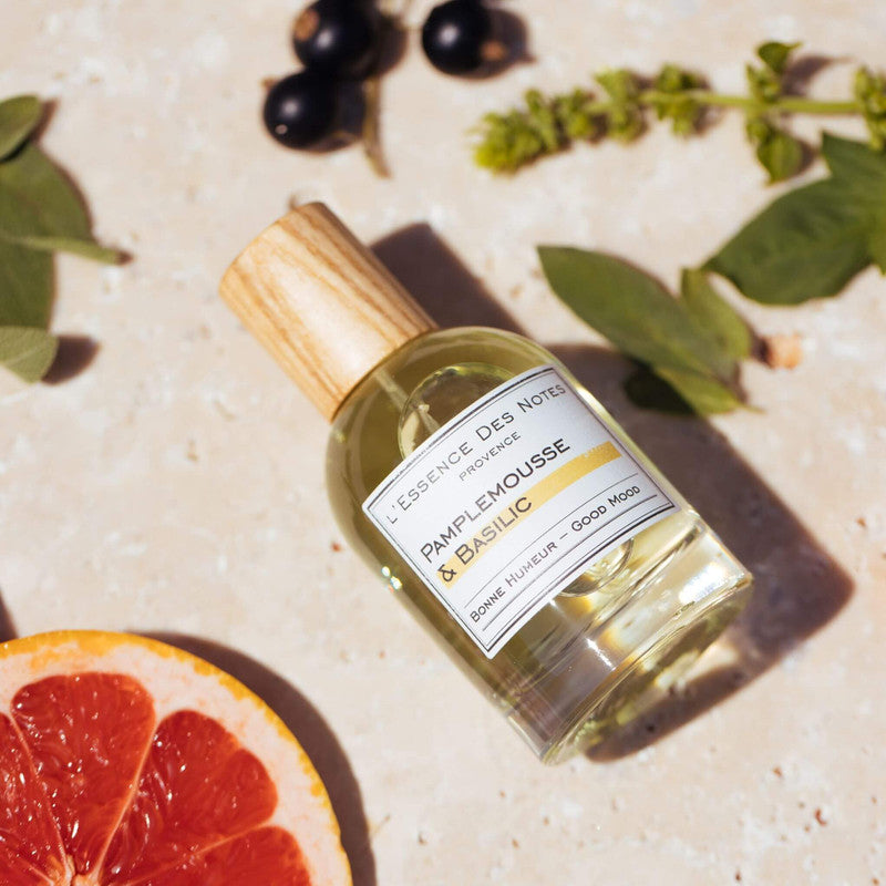 Perfume Pamplemousse L'Essence des Notes sobre fondo claro junto a ingredientes