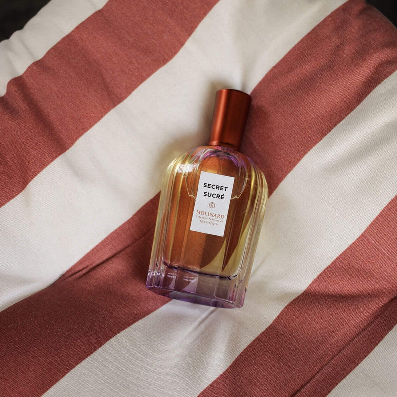 Perfume Secret Sucré sobre cojín con rayas blancas y rosas
