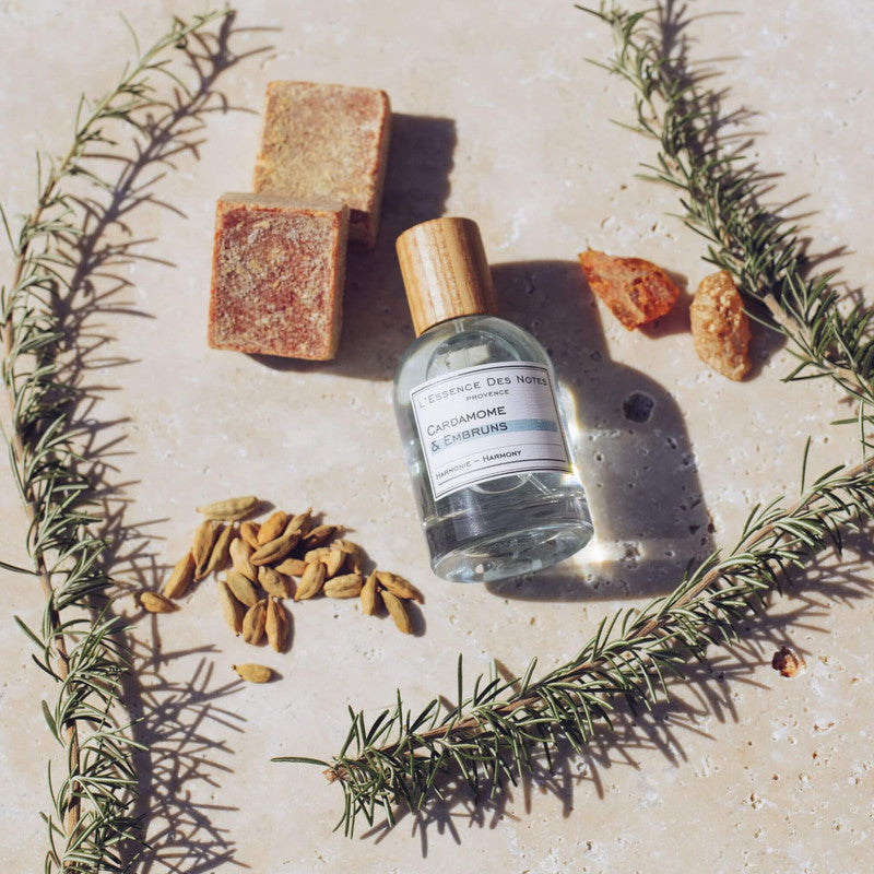 Perfume Cardamome & Romarin de L'Essence des notes sobre fondo de piedra beige junto a especies e ingredientes