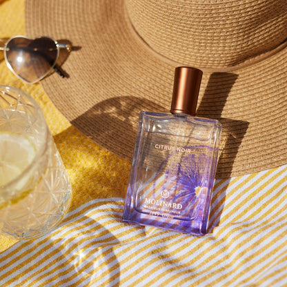 Perfume Citrus Noir al sol con fondo amarillo playero