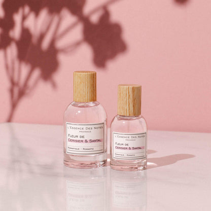 Perfume Fleur de Cerisier & Santal de L'Essence des notes 2 botellas sobre base de marmol con pared rosada y sombra de flores