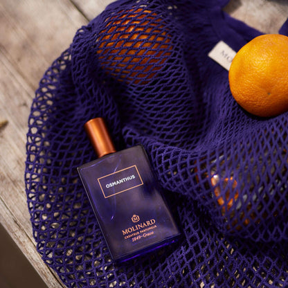 Perfume Osmanthus de Galimard sobre bolsa de red morada con naranjas