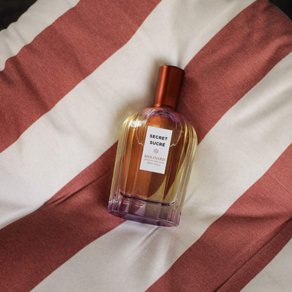 Perfume Secret Sucré sobre cojín con rayas blancas y rosas