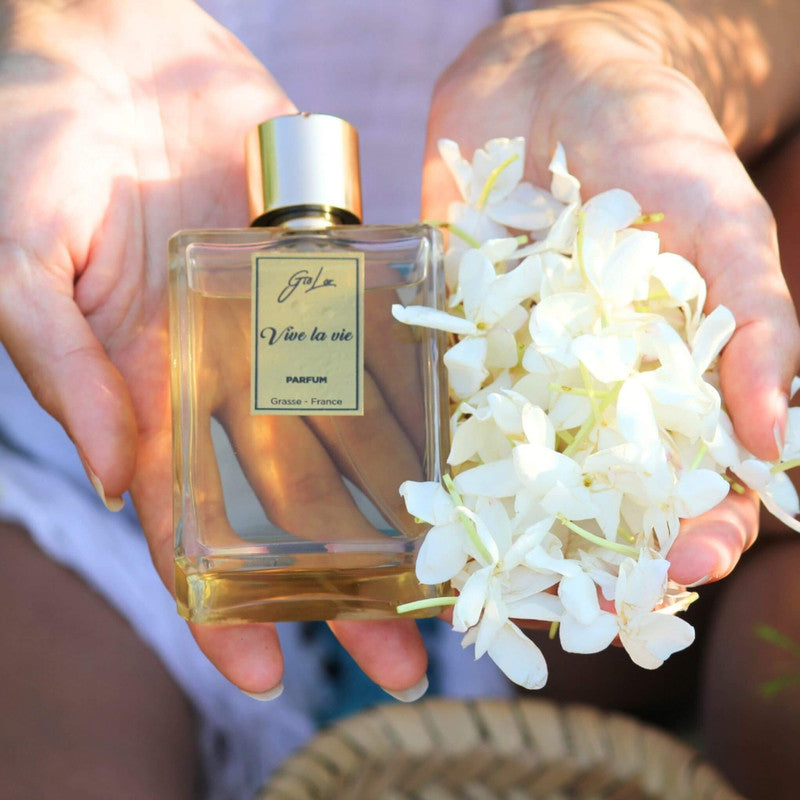 Perfume Vive la Vie de Giolor en manos de una mujer junto a flores de jazmin